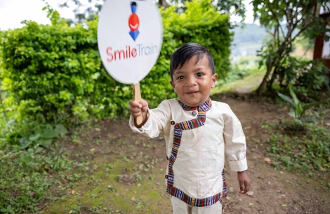 Asher smiling and holding a Smile Train sign