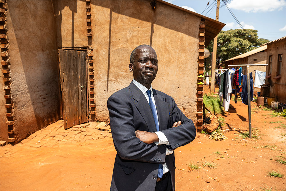Mandigaisa standing in a suit in front of his house with his arms crossed proudly